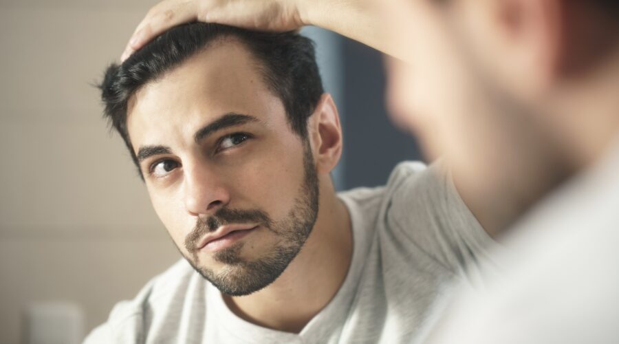 man looking at his hair in mirror as Amazon launches new hair loss and acne clinic